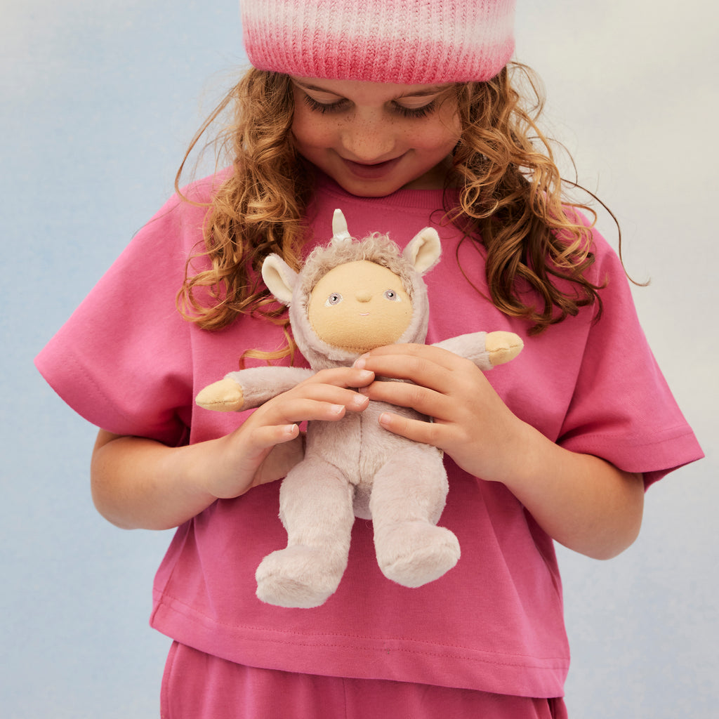 Child holding Uma Unicorn doll while smiling – Young girl in pink shirt cuddling a lilac plush unicorn doll with silver horn.