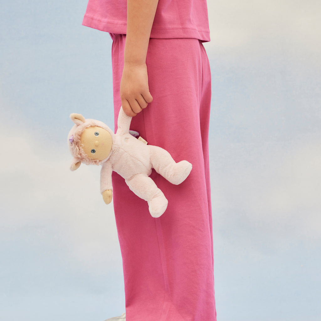 Person holding Una Unicorn by the arm – doll dangling playfully against a blue sky background.