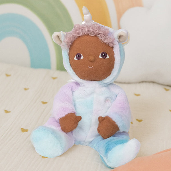 Uli Unicorn Doll against rainbow backdrop – Plush Dinkum unicorn doll seated on a pastel rainbow background with confetti.