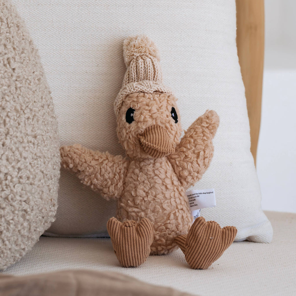 Edmond Duck soft toy propped on a white pillow, highlighting plush cotton texture and caramel corduroy accents.
