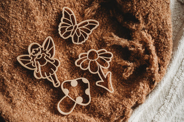 Flat lay of 4-piece Kinfolk Pantry Fairytale Cutter Set on soft brown fabric, featuring butterfly, flower, fairy, and mushroom shapes.