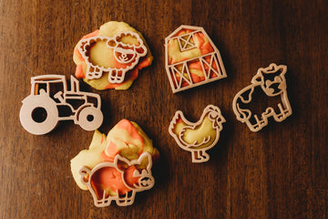 Flat lay of Kinfolk Pantry Mini Farm Cutter Set on wood background, featuring barn, sheep, pig, cow, tractor, and chook shapes.