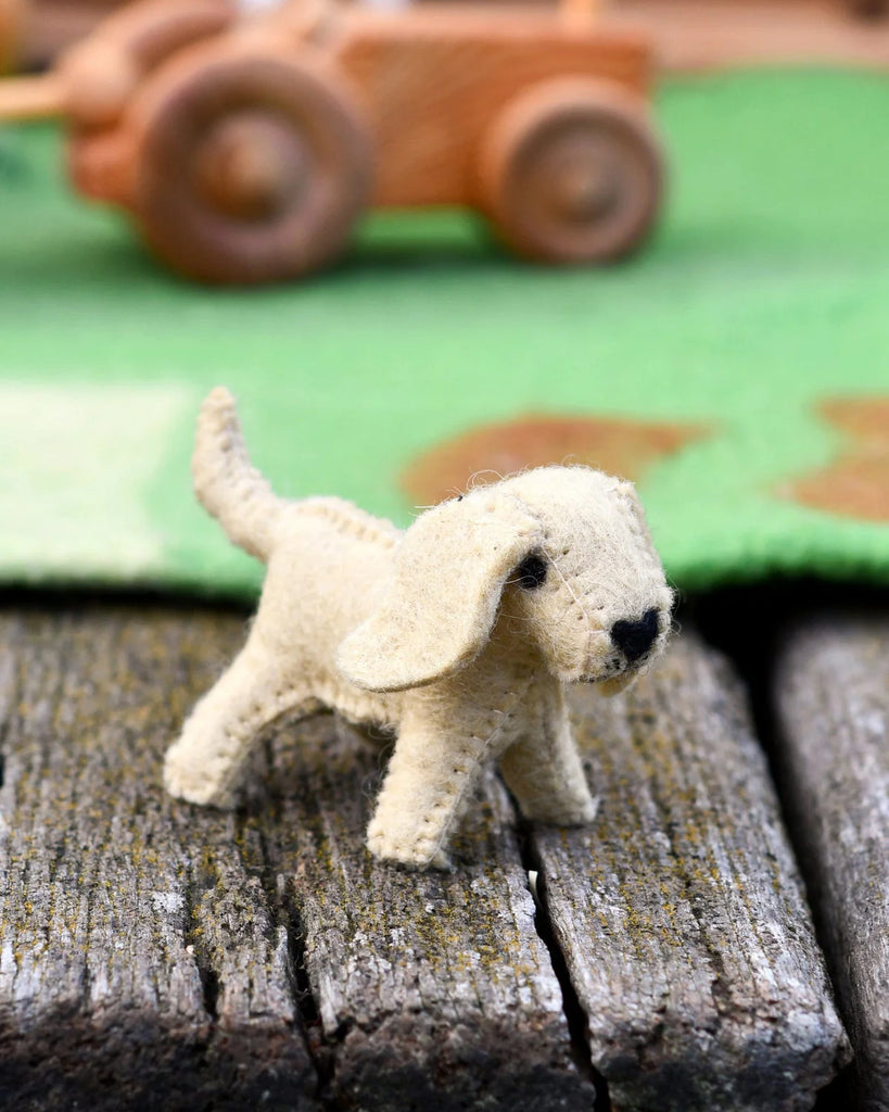 Handmade cream felt dog toy with floppy ears and stitched details, standing on a wooden surface with a green felt play mat behind it.