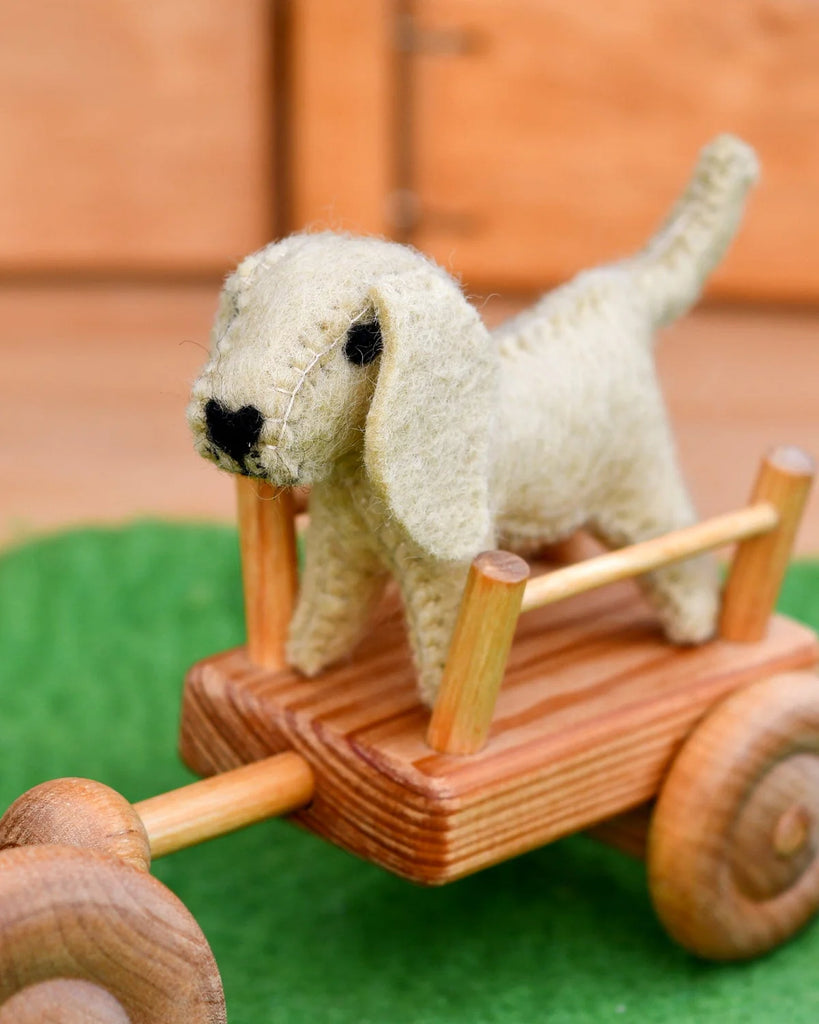 Felt dog toy sitting in a miniature wooden wagon, part of a whimsical small world farm play setup.