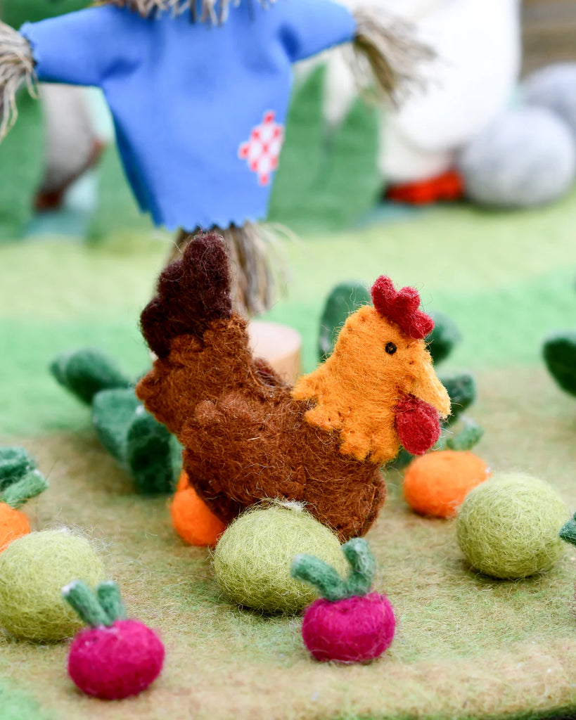 Felt chicken toy surrounded by colourful felt play balls, posed on a green play mat with a miniature farm scene in the background.