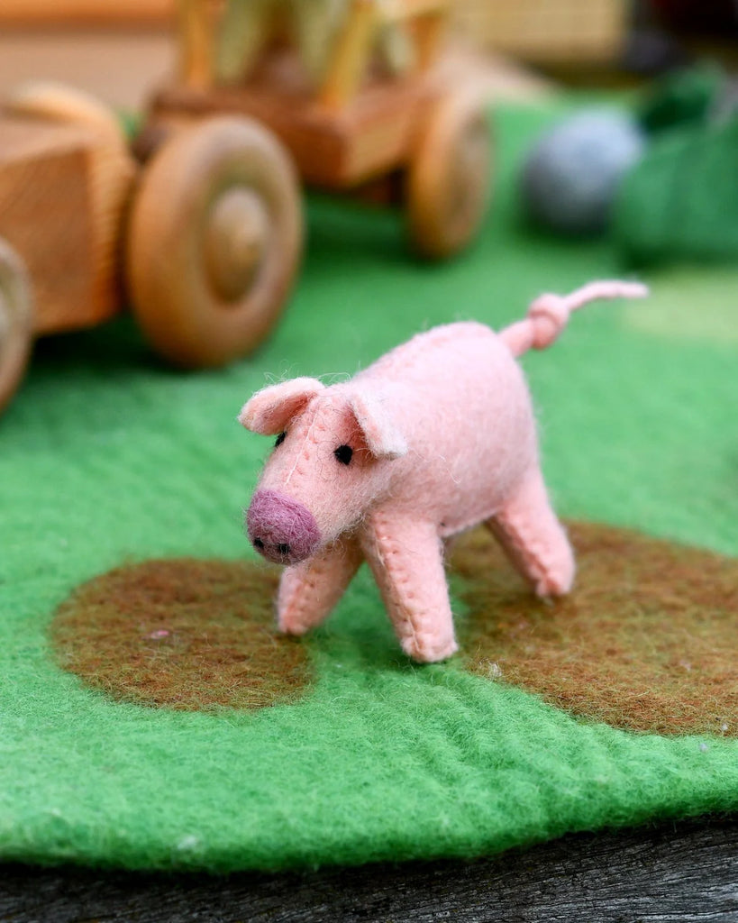 Pink felt pig farm toy on a play mat, with wooden toys and felt grass patches creating a small world imaginative play scene.