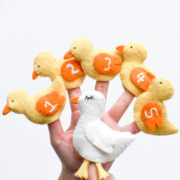 Hand holding a full set of felt finger puppets including one white mother duck and five yellow ducklings numbered 1 to 5.