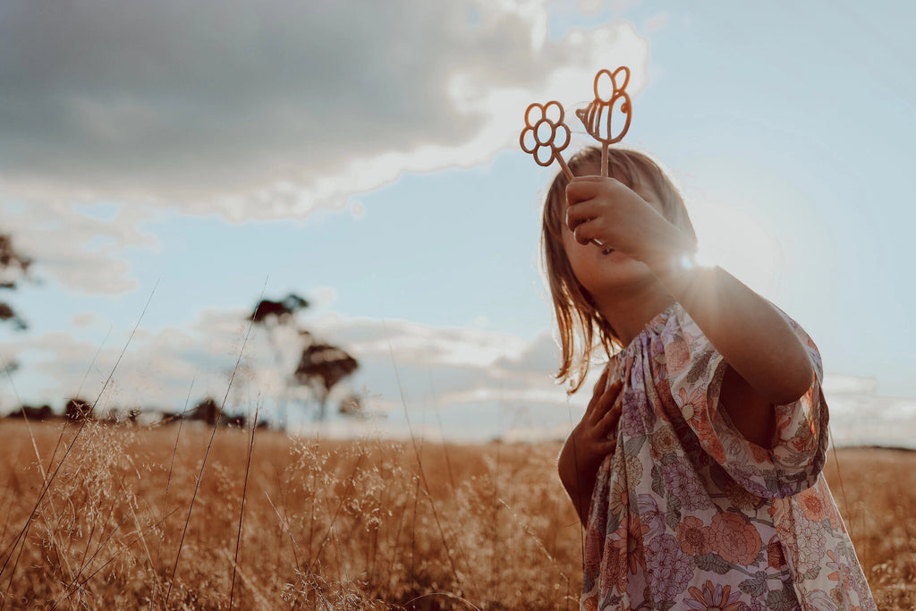 Child playing with flower-shaped eco bubble wand outdoors in nature during golden hour.