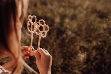 Close-up of Kinfolk Pantry Flower Eco Bubble Wands (Flower & Bee Designs) held by a child in a sunlit field, made from recycled sawdust and PLA bioplastic.