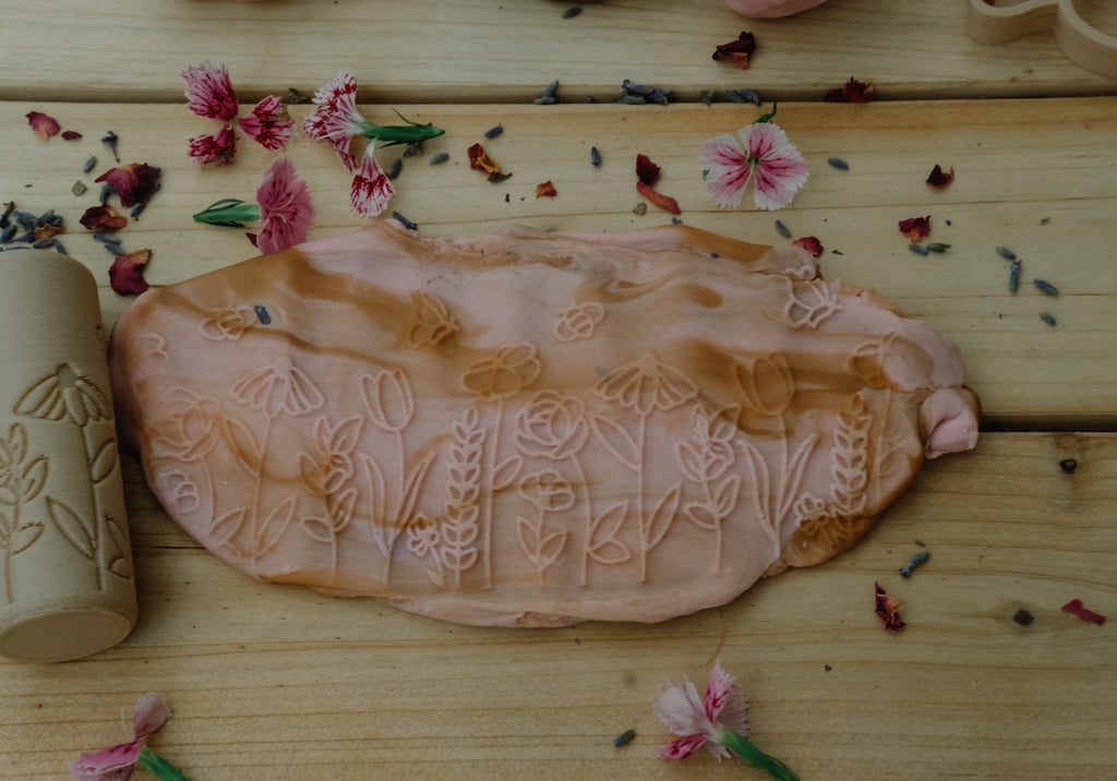 Flat lay of pink playdough with pressed flower impressions, surrounded by real petals, created with eco-friendly floral roller.