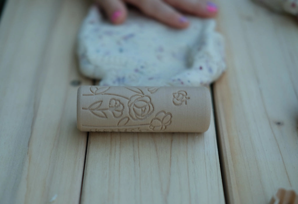 Child rolling Kinfolk Pantry Flower Roller across floral-infused white playdough, creating delicate flower impressions.