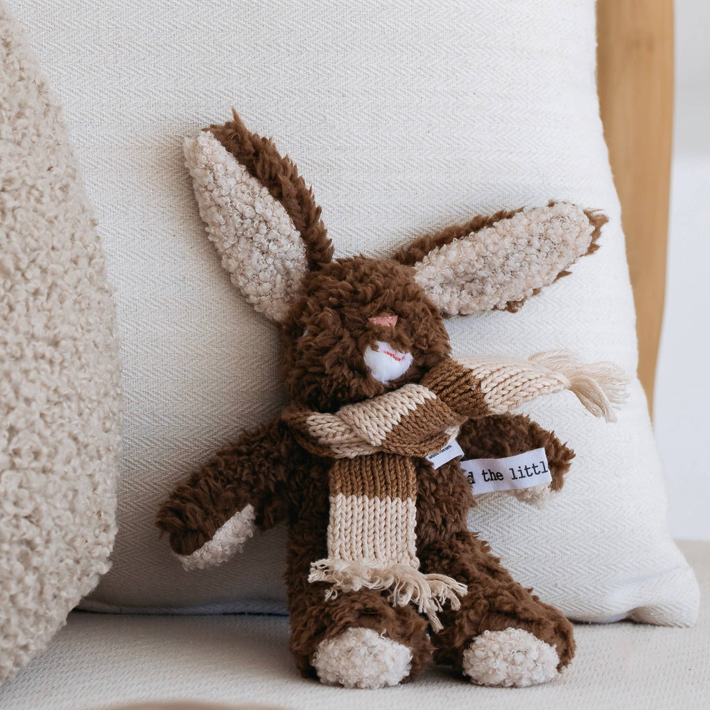Frankie Rabbit mini plush toy sitting upright on a white cushion, showing long floppy ears, stitched face, and fringed wool scarf.