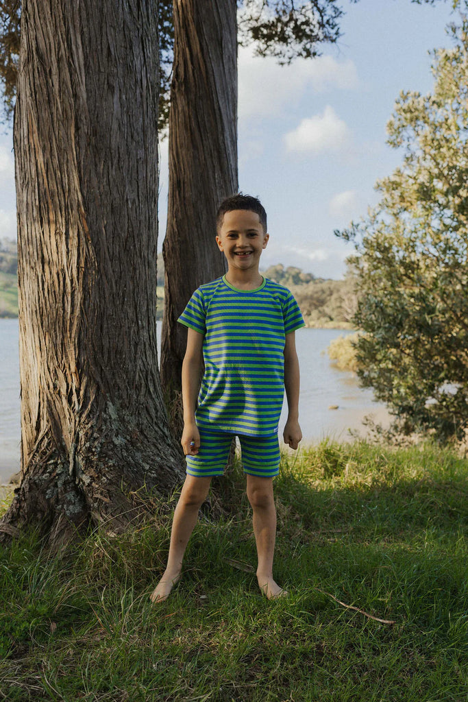 Child in a striped outfit standing next to a tree by a body of water