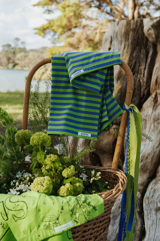 Green and blue striped towel draped over a wicker basket with flowers, against a natural background.