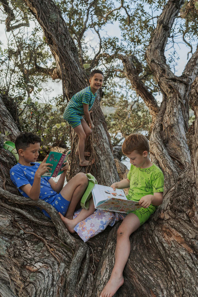 Three children sitting in a large tree, reading books.