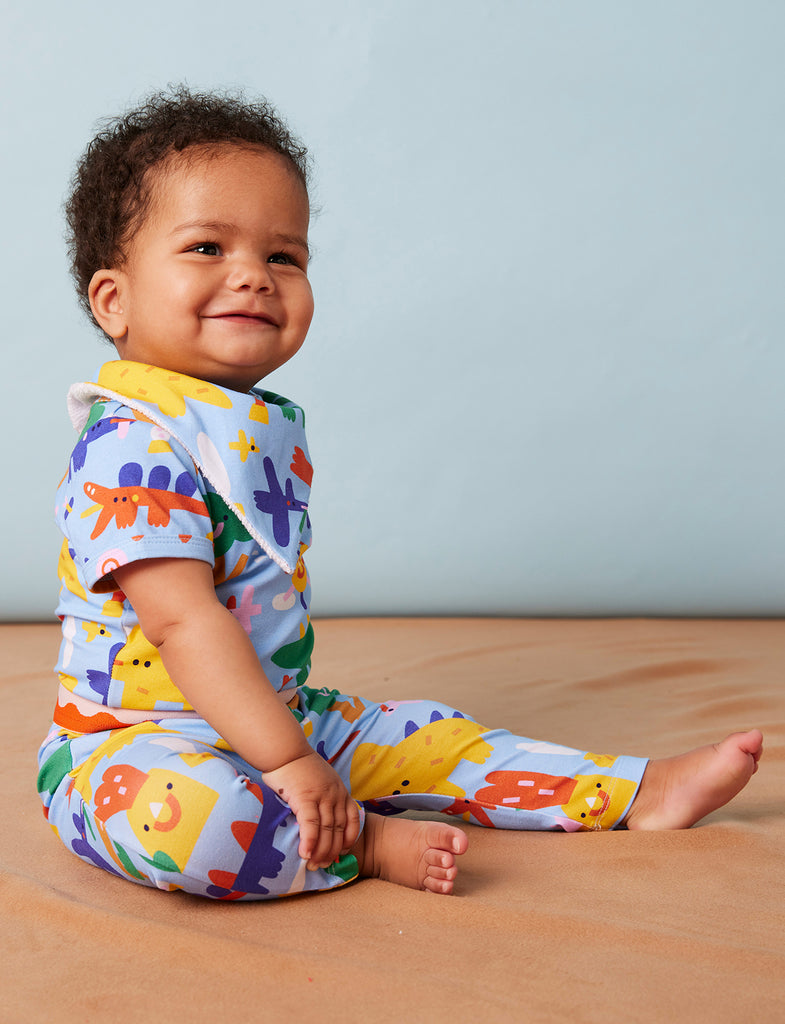 Smiling baby sitting in Dino Days leggings and matching top, showing off the vibrant print and comfy fit of the Halcyon Nights babywear set.