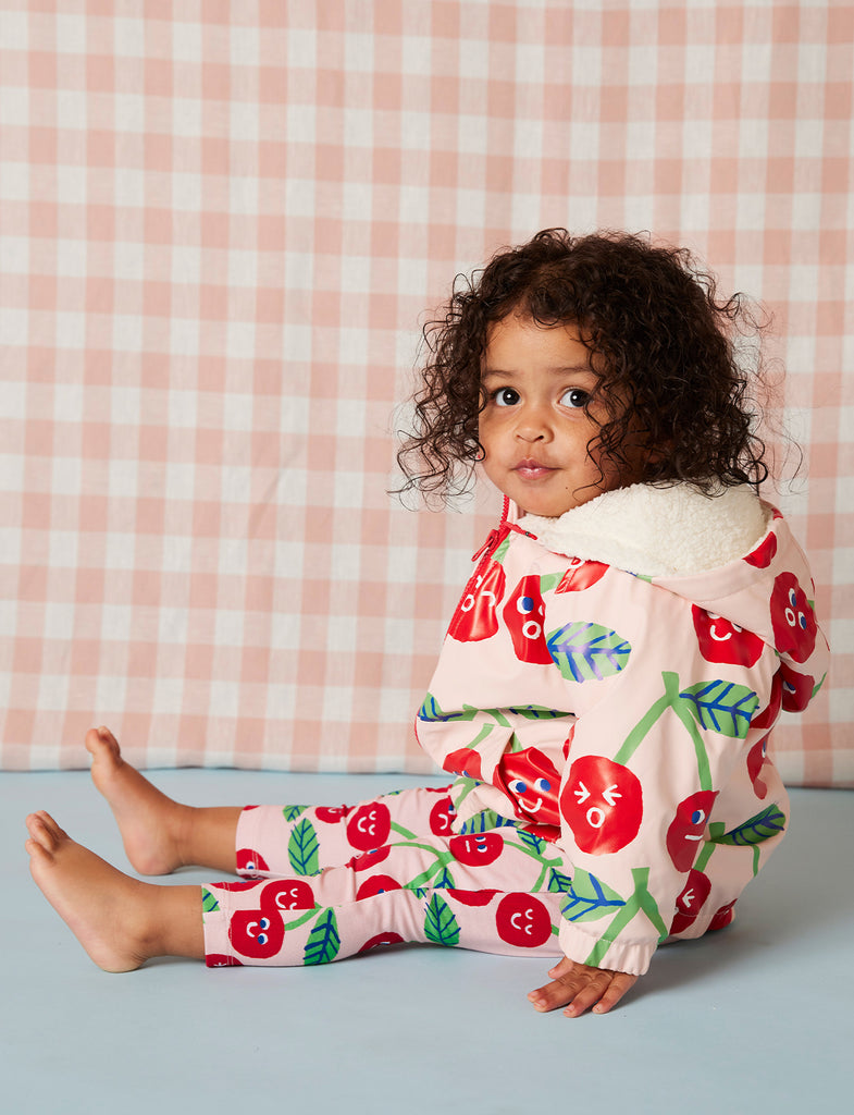 Toddler wearing Cheeky Cherry leggings and matching top, sitting sideways and showing relaxed fit and bright cherry-themed design.
