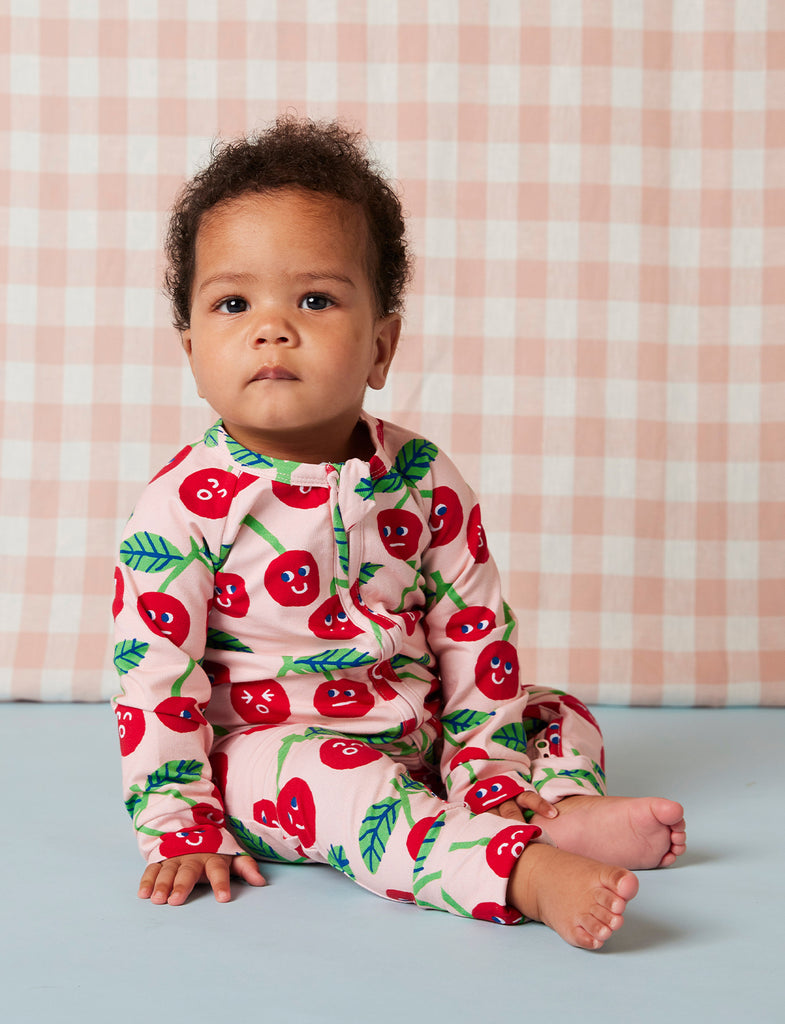 Baby sitting in Cheeky Cherry romper by Halcyon Nights, showing relaxed fit and fun cherry pattern on soft, breathable cotton fabric.
