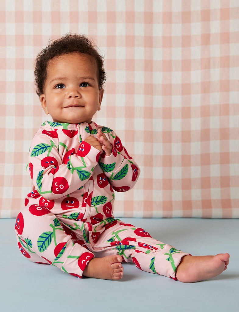 Side view of baby in Cheeky Cherry romper, featuring playful cherry design, fold-over foot cuffs, and comfy fit perfect for cooler weather.
