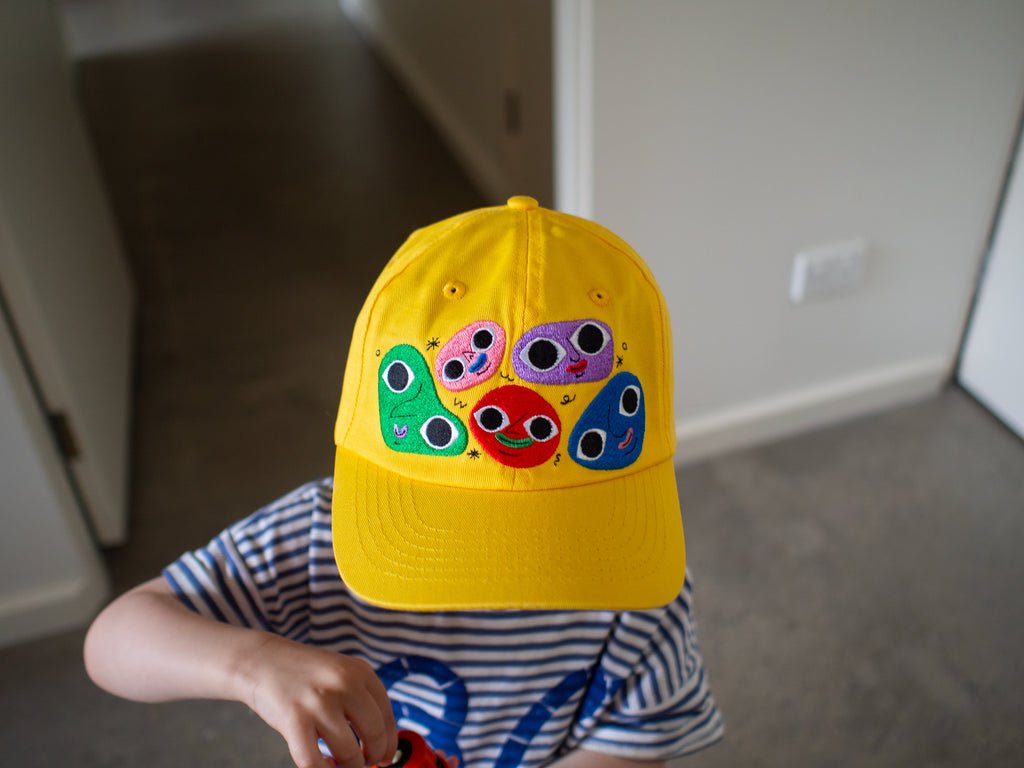Cheerful yellow cotton twill cap, the Happy Chap Cap, designed by Melbourne illustrator Samantha Curcio. Features playful embroidered details, perfect for kids aged 2+.