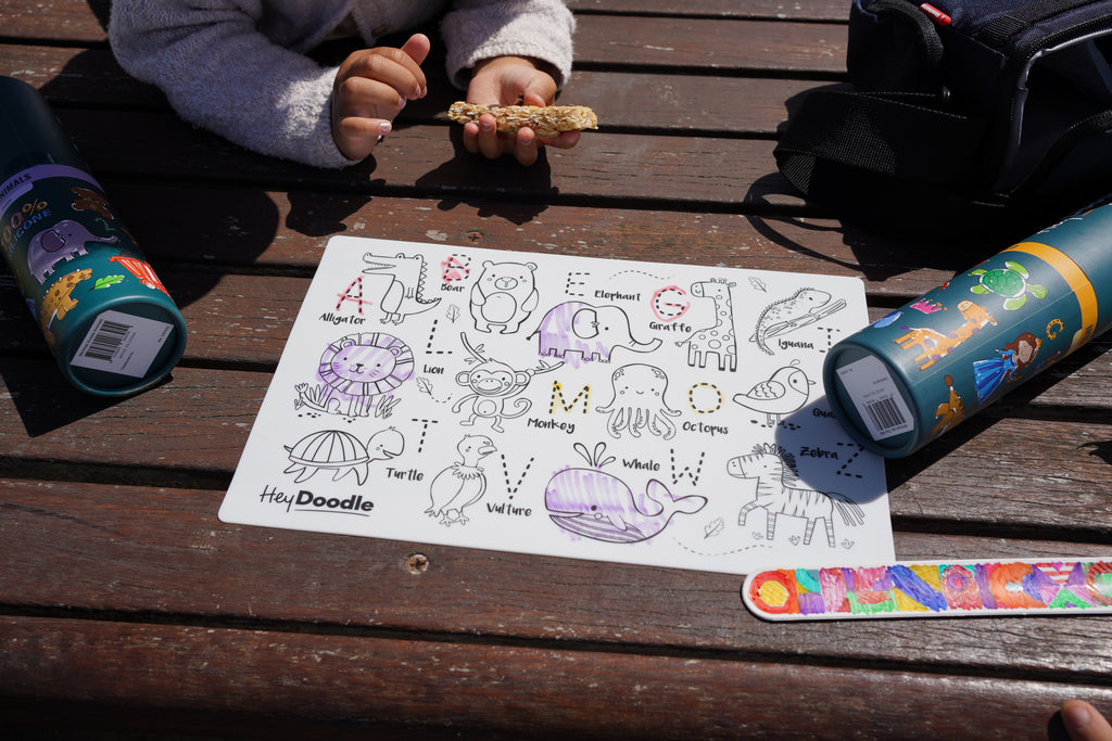 Two children using HeyDoodle Into the Wild mini mat at a picnic table outdoors.