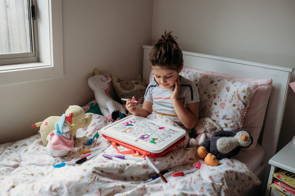Close-up of child colouring the washable alphabet mat in a cozy bedroom setting.