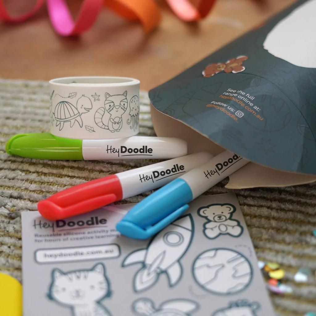 Close-up view of a child using red, green and black mini markers to colour a HeyDoodle Sketchband and sticker sheet.