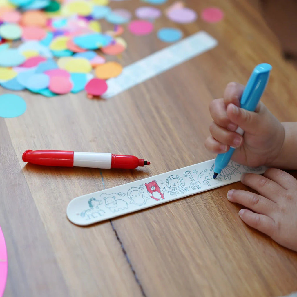 Child assembling a Sketchband gift pack with colourful mini markers and fun accessories on a wooden table.