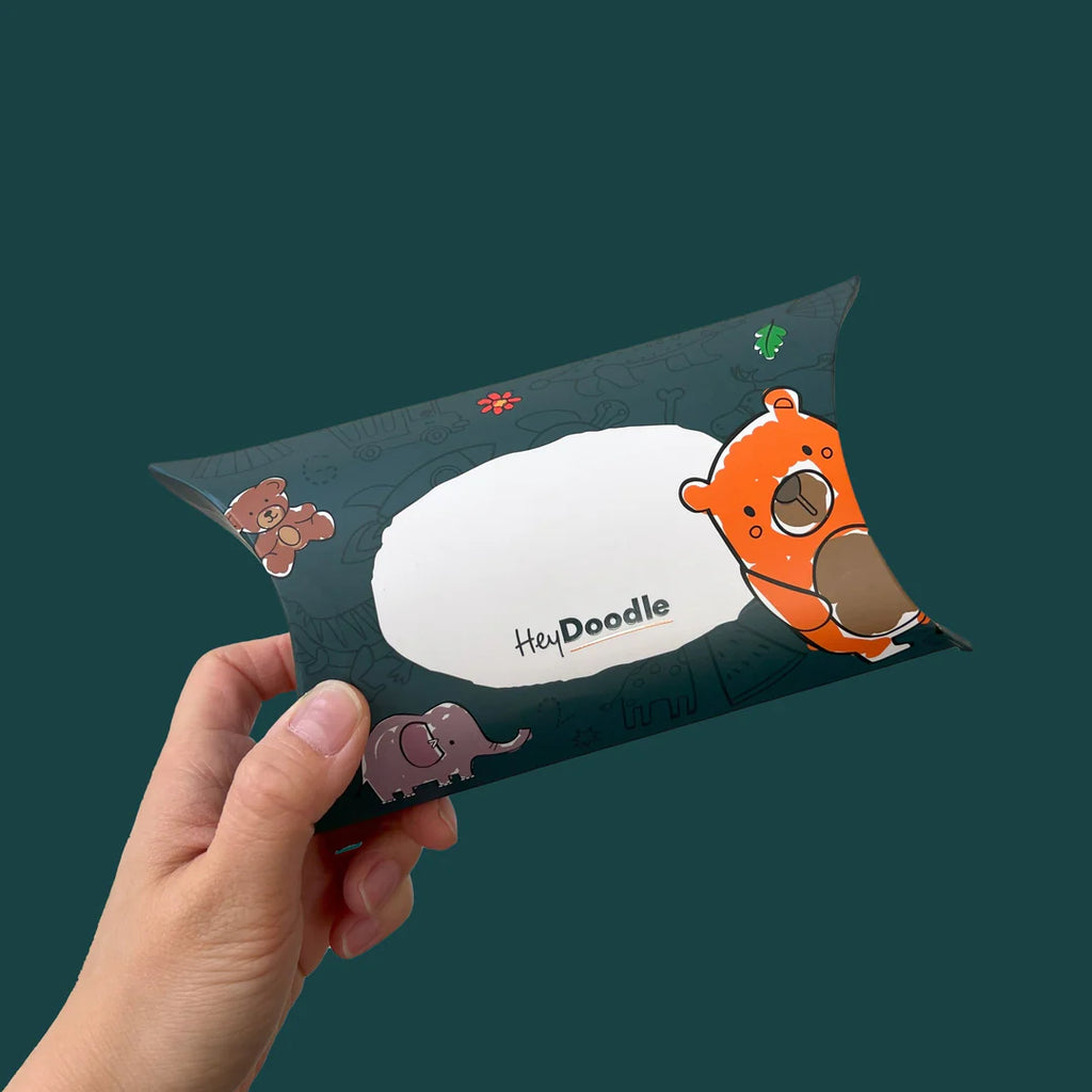 Hand holding a completed HeyDoodle Sketchband favour box with colourful design and character illustrations.