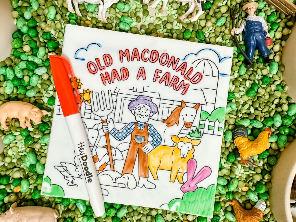 Colourful Old MacDonald silicone storybook displayed with farm-themed figures and markers in a sensory table.
