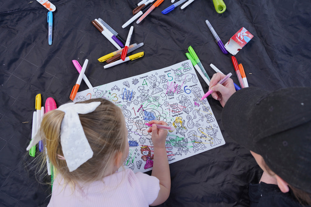 Two children colouring the HeyDoodle Sugar and Spice silicone mat outdoors with colourful markers.