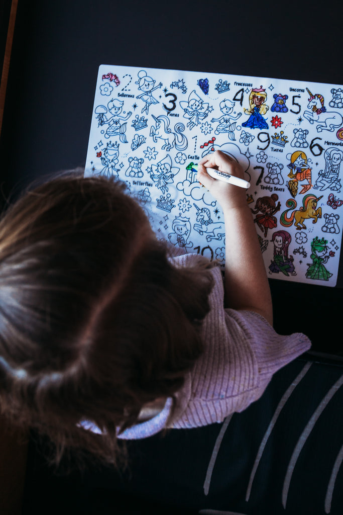 Overhead view of child colouring fairy and unicorn illustrations on the Sugar and Spice mat.