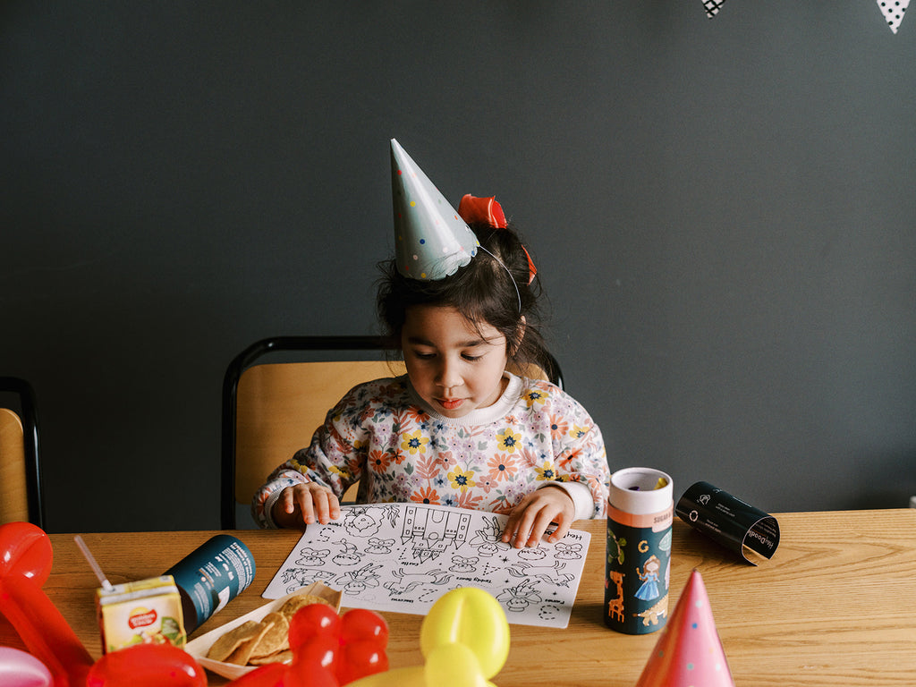 Child smiling and colouring HeyDoodle Sugar & Spice mini mat at a party table.