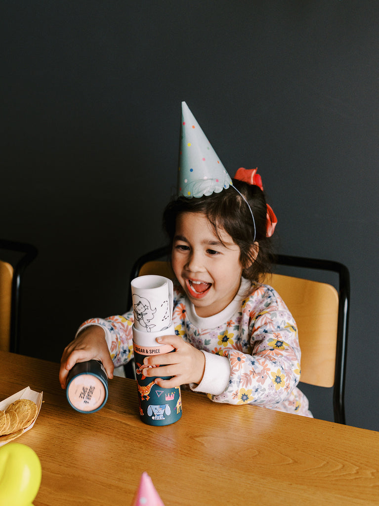Girl wearing a party hat, proudly holding up the Sugar & Spice mat at a birthday celebration.