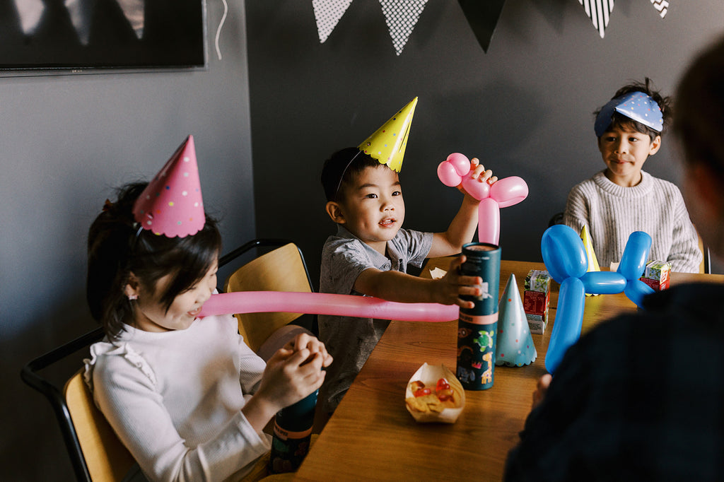 Children gathered at a birthday table colouring Sugar & Spice HeyDoodle mats together under party bunting.