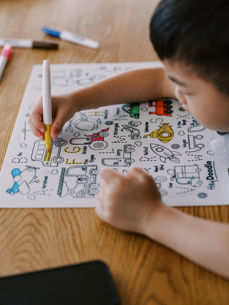 Child colouring HeyDoodle Toot Toot Honk transport mat at a wooden table.