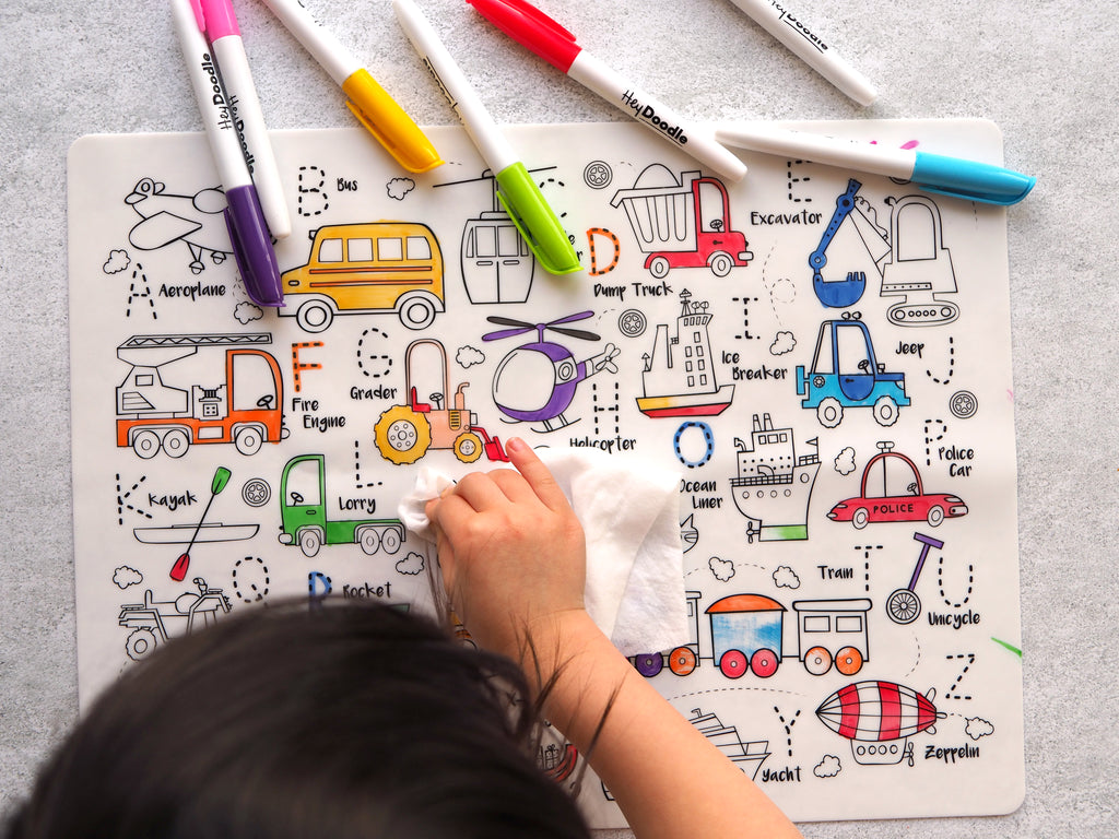 Child wiping clean the HeyDoodle transport-themed mat after use with a damp cloth.