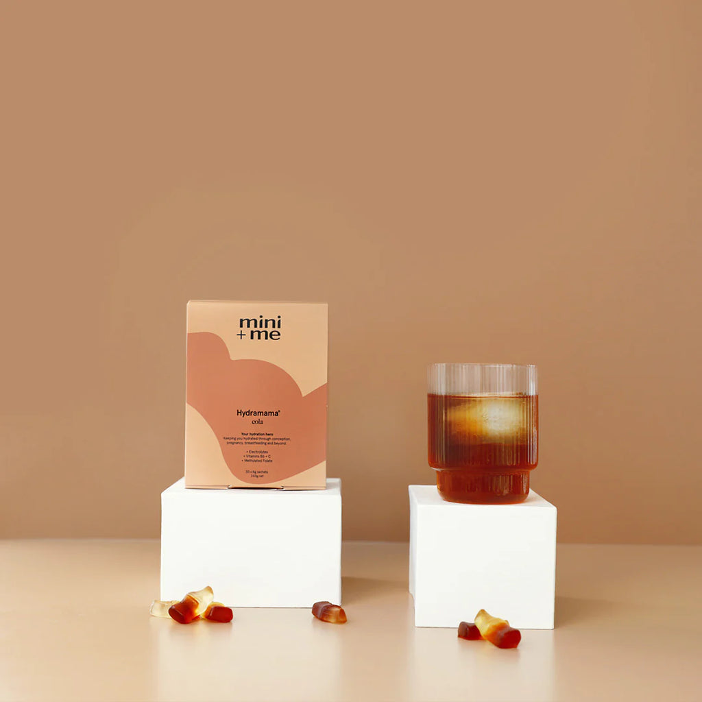 Hydramama Cola - Hydration Electrolyte Drink for Pregnancy & Postpartum - Hydramama box pictured next to a hydramama drink in a gass with ice and cola gummies scattered.