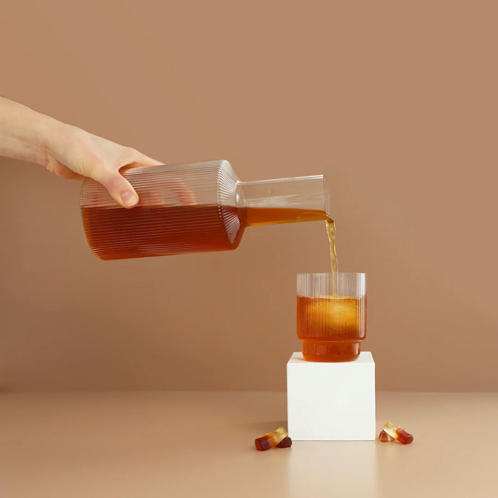 Hydramama Cola - Hydration Electrolyte Drink for Pregnancy & Postpartum - Hydramama Drink being poured from jug into glass with ice and cola gummies scattered around.