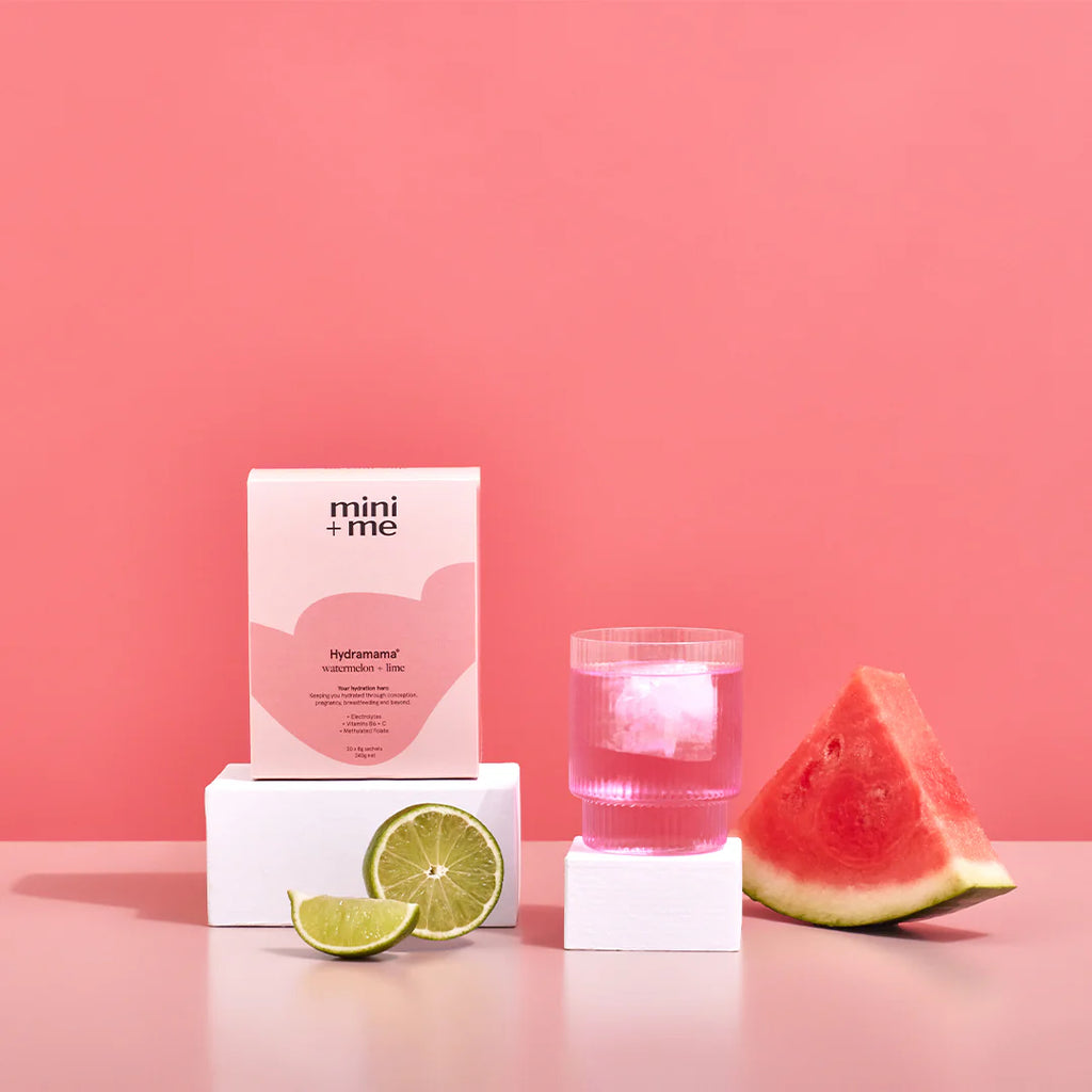 Hydramama Watermelon & Lime box and sachet displayed with a glass of pink drink, lime slices, and watermelon pieces on a pink background.