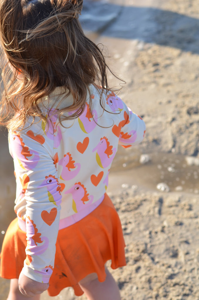 Bubblegum swim skort with tangerine ribbed shorts and a light pink skirt overlay, featuring UPF 50+ protection and a beige lining. Fun and flouncy design, perfect for sunny beach or pool days.