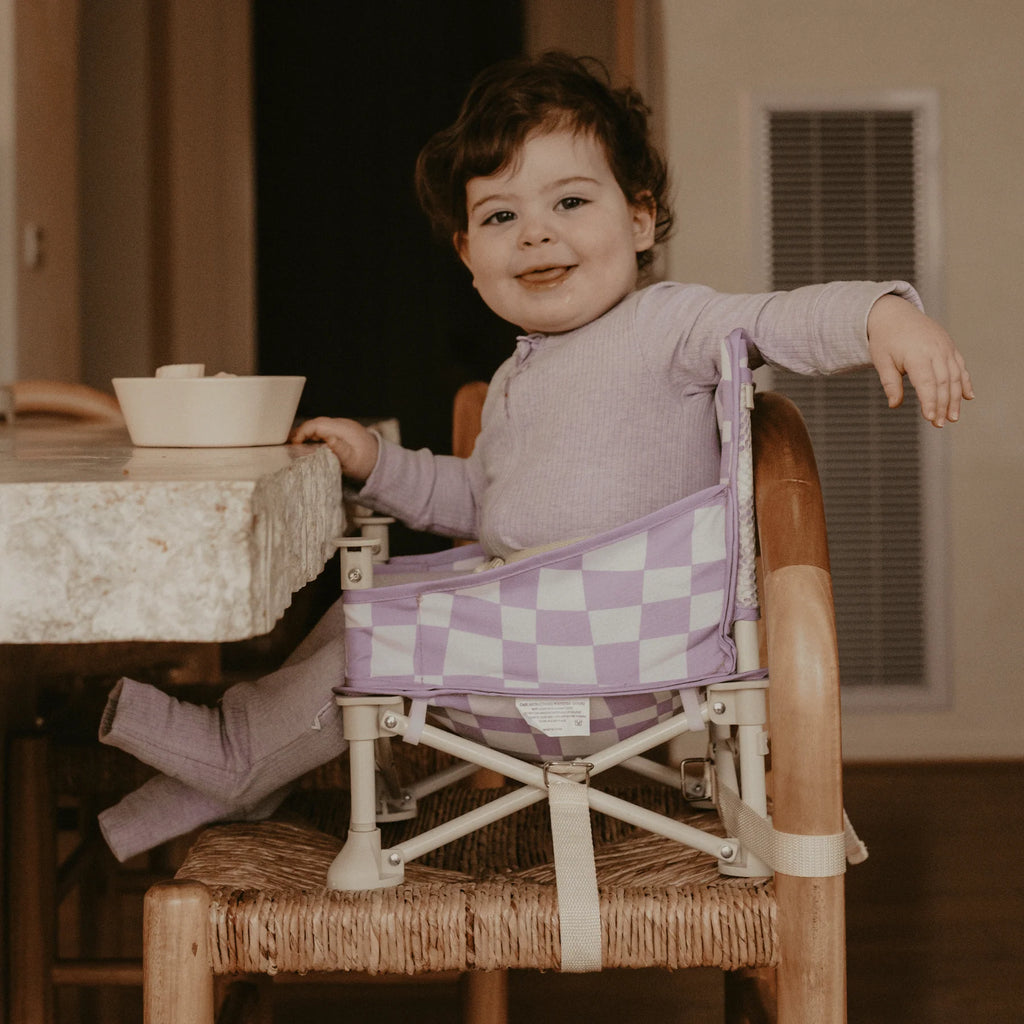 Baby sitting in Izimini Ava Baby Chair at a dining table wearing matching lilac outfit.