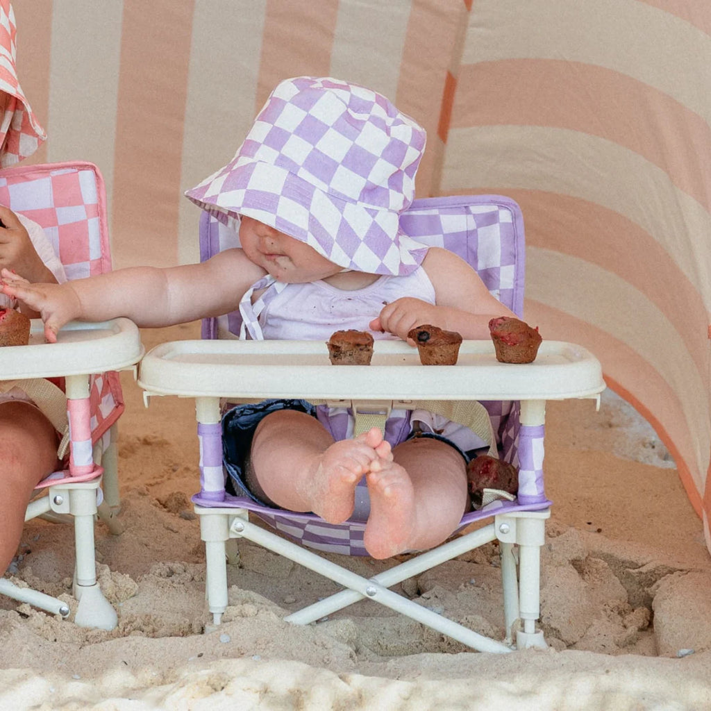Baby sitting on the beach using the Izimini Ava Baby Chair with snack tray and checkered pattern.