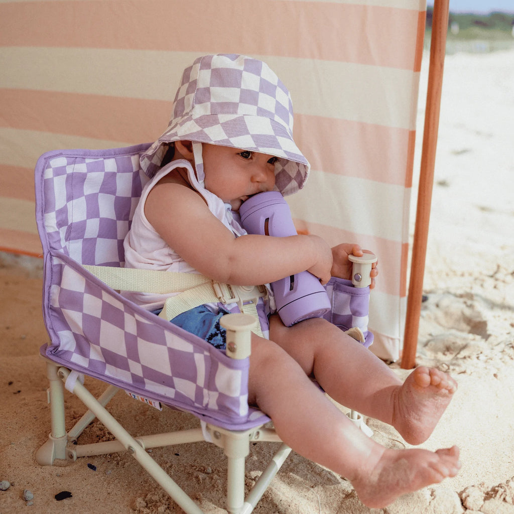 Baby drinking from a bottle while seated in the Izimini Ava Baby Chair under a beach shade.