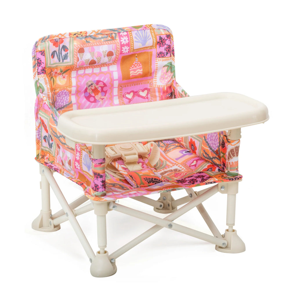 A foldable baby booster chair with a colorful Amy print featuring pink, orange, and purple patchwork patterns, and a detachable white tray.