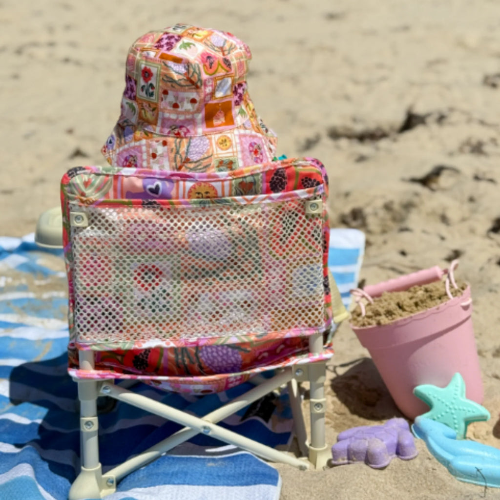 Rear view of the Izimini Baby Chair with a mesh back and Amy print, placed on a beach towel beside sand toys.