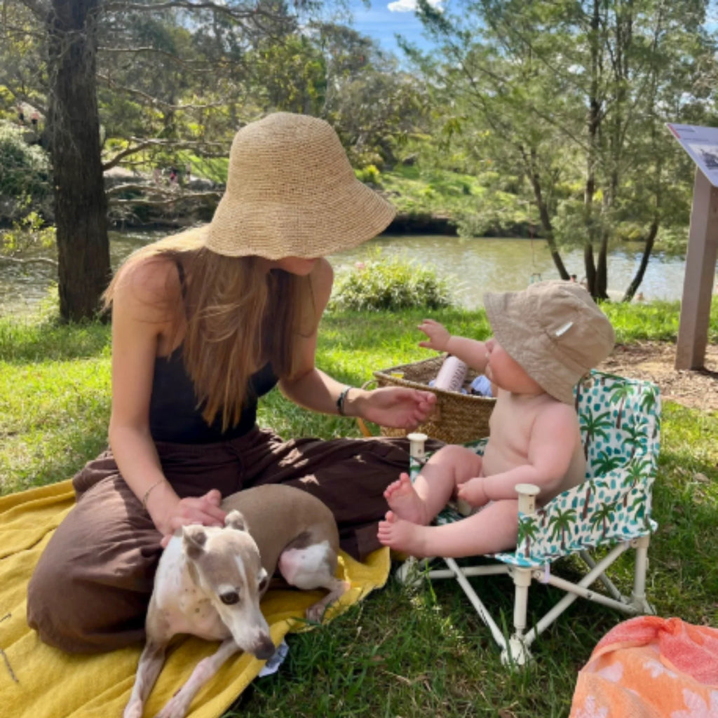 Mother and baby enjoying picnic with Izimini Baby Chair Kai – portable high chair with safety harness, ideal for outdoor adventures.