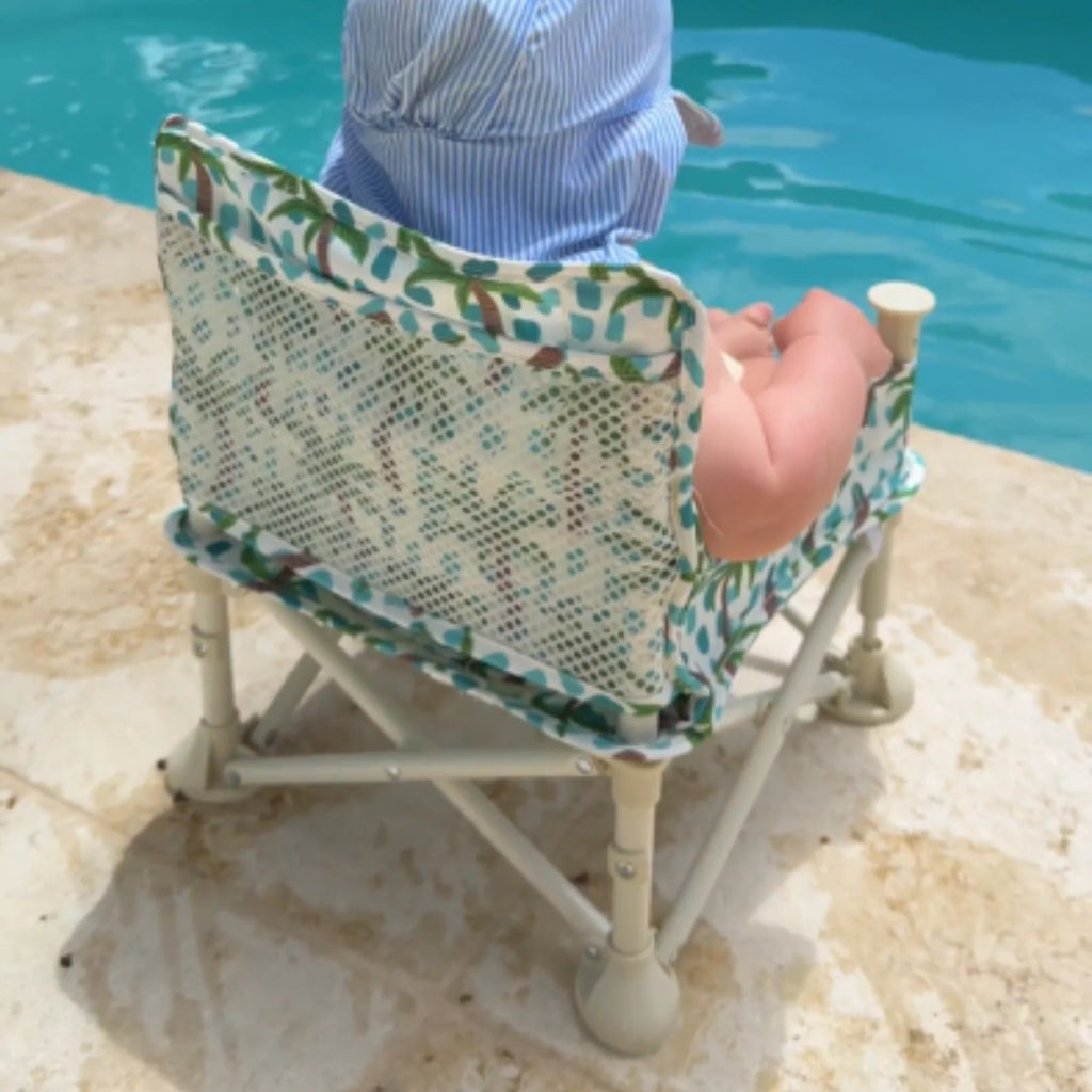 Baby relaxing in Izimini Baby Chair Kai tropical print chair by the pool – lightweight travel chair for feeding and playtime.