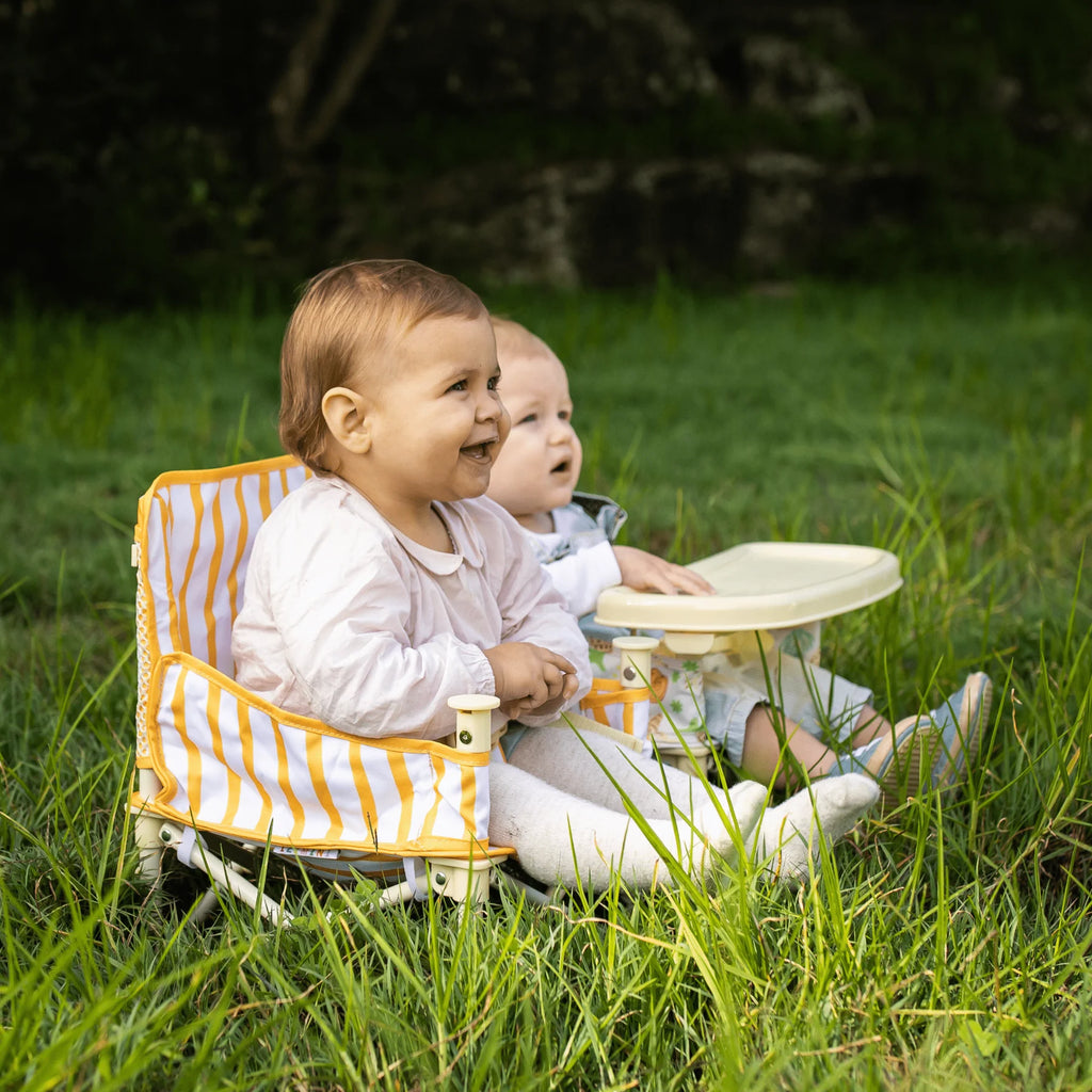 Two babies sitting in Izimini Brighton baby chairs in the grass, smiling and playing during outdoor time.