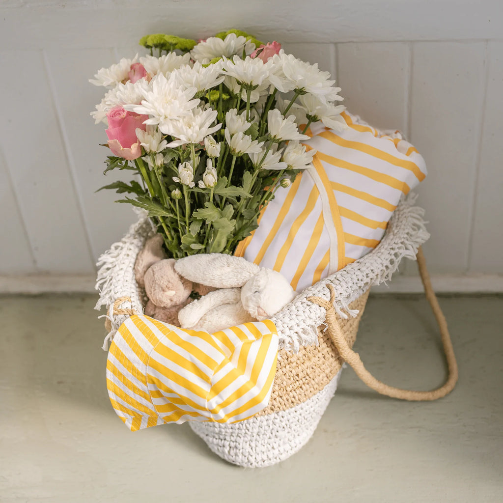 Yellow and white striped Izimini Brighton chair fabric and matching hat placed in a woven basket with flowers.